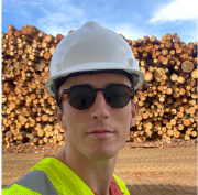 Sean Treacy standing in front of lumber materials with a hardhat and high-visibility vest.