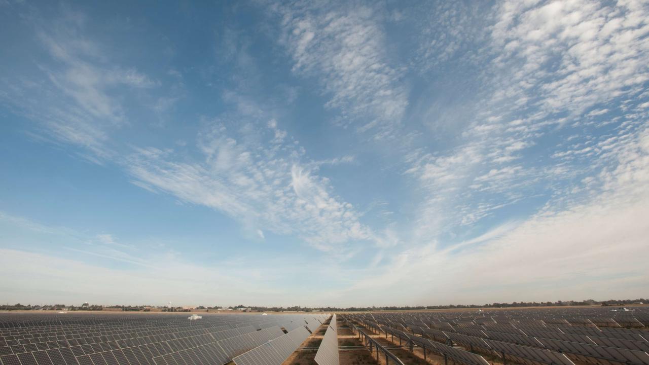 Photo of a solar farm with blue sky filled with clouds.