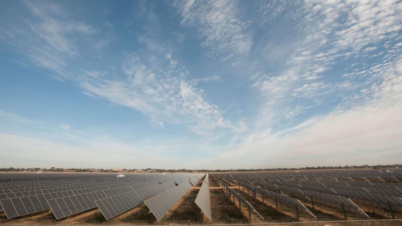 Photo of a solar farm with blue sky filled with clouds.