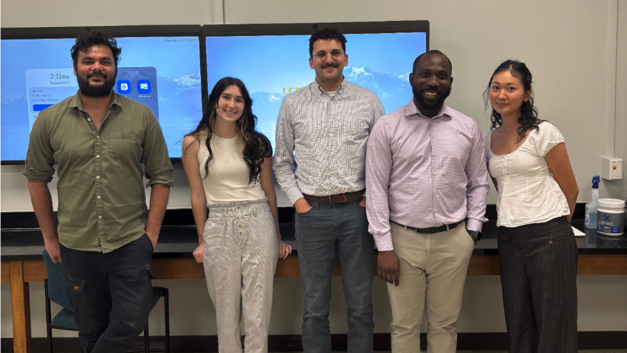 Five smiling adults standing before monitors in a classroom