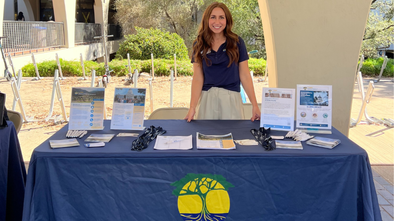 Jessica Penrose featured in front of a recruitment table with the program's name on it.