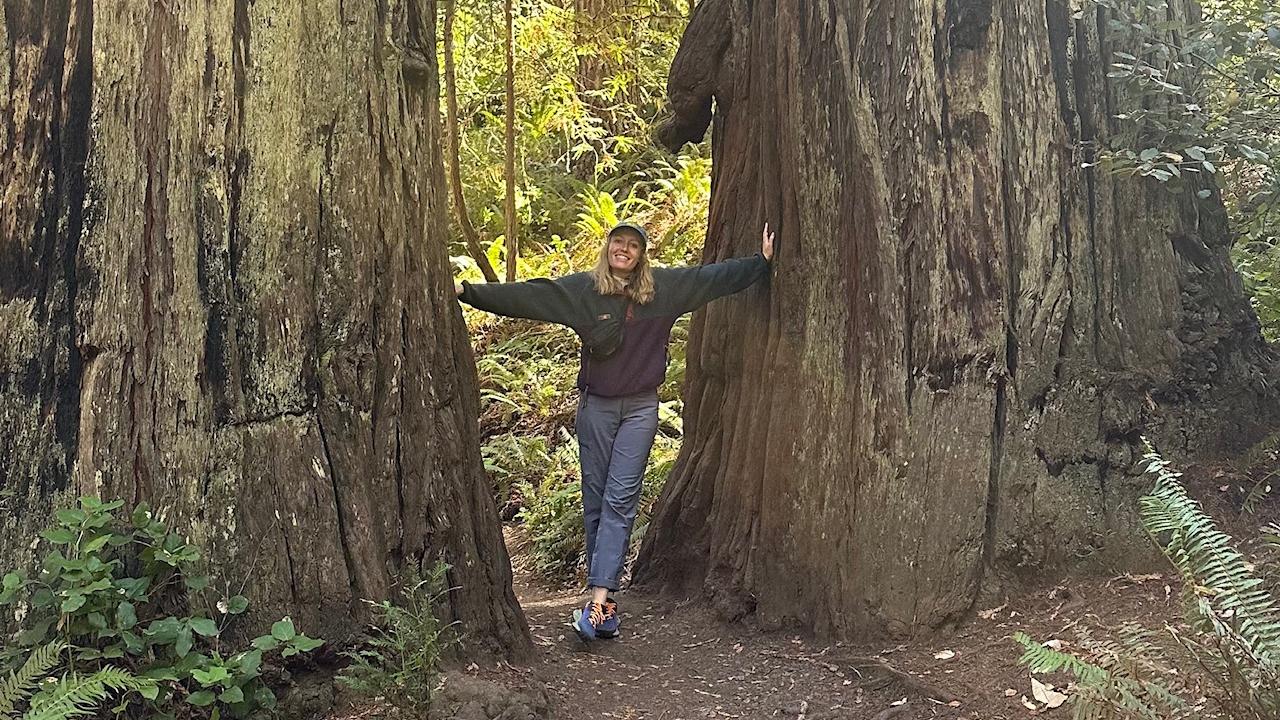 Kaitlyn Finlayson smiling in the middle of two large trees.