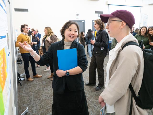 JieQi Yan talking with a student, pointing to a poster board with details of her completed project.