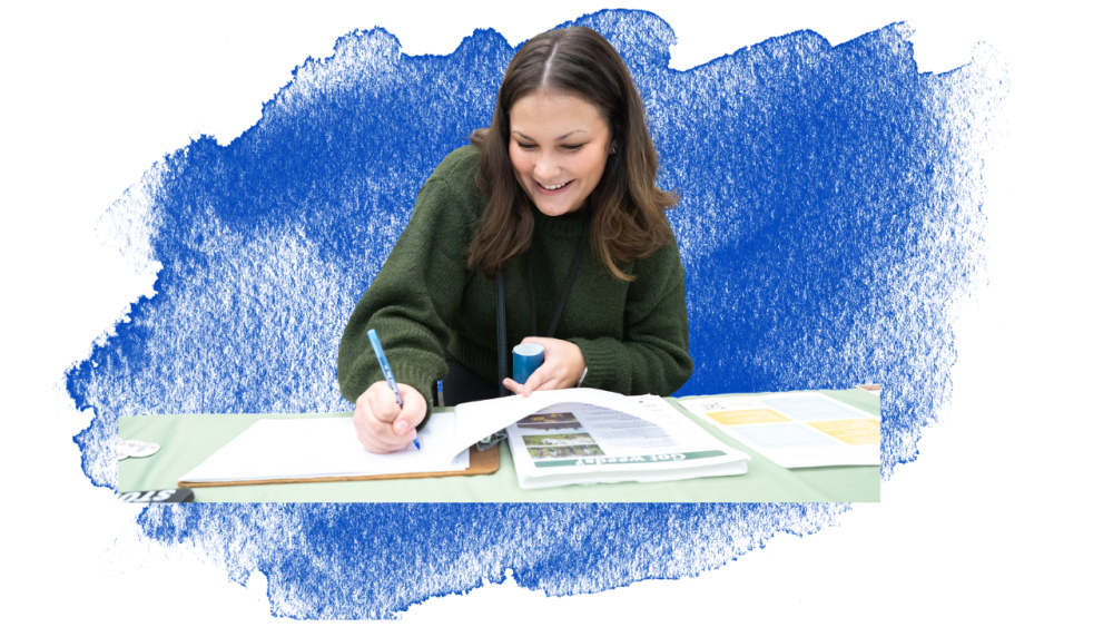 Courtney Carpenter featured smiling and writing something on a clipboard on a table.