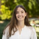 Young woman with long brown hair smiling in white blouse, blurred green garden background