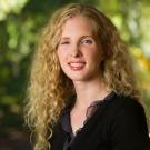 Headshot photo of smiling young woman with long curly blonde hair, green blurred background